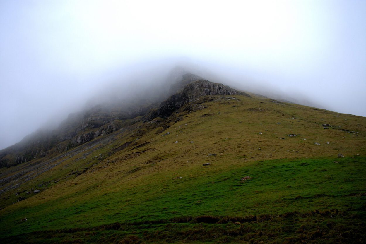 Ein grasbewachsener Hügel mit einem Berg im Hintergrund.