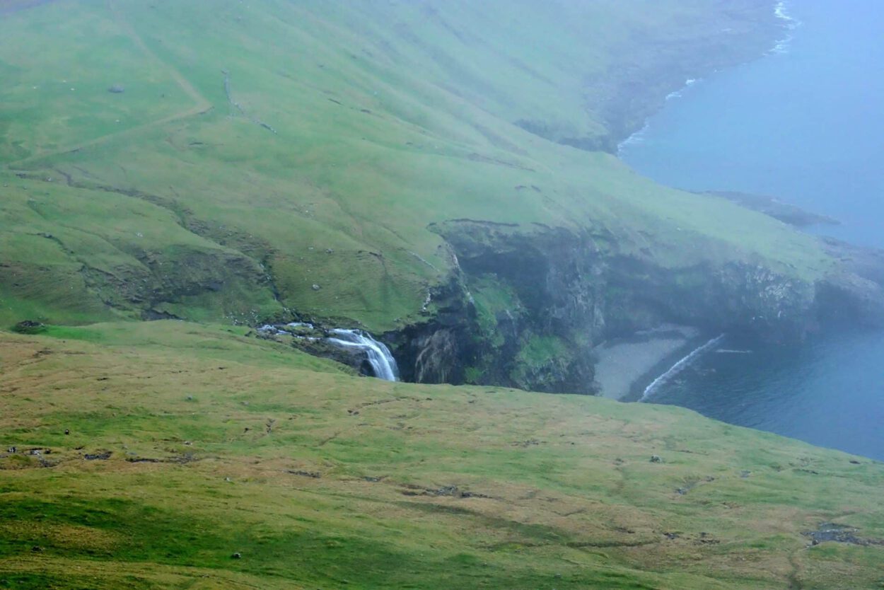 Ein Wasserfall auf einem grünen Hügel in der Nähe des Ozeans.