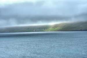 Ein bewölkter Himmel über einem Gewässer mit einem Hügel im Hintergrund.