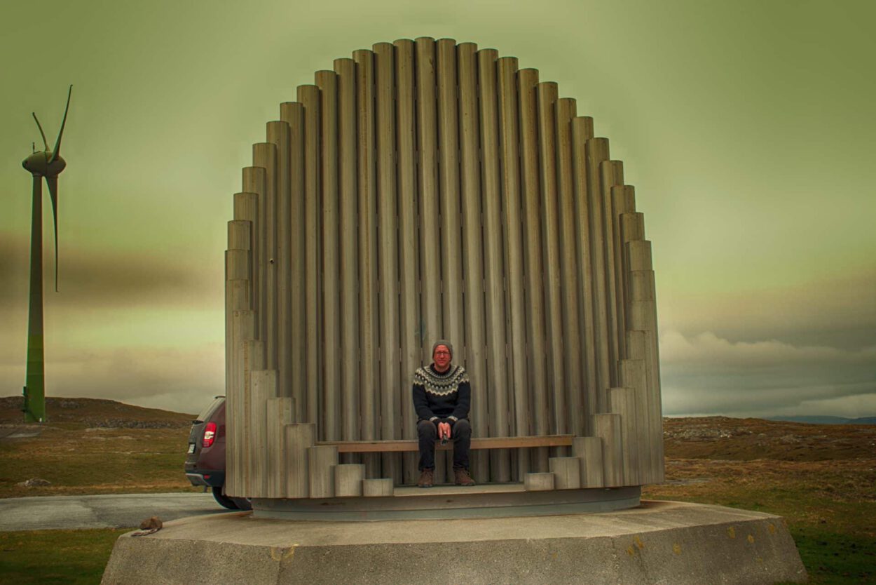 Eine Frau sitzt auf einer Bank vor einer Windkraftanlage.