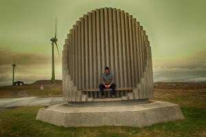 Ein Mann sitzt auf einer Bank vor einer Windkraftanlage.