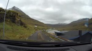 Ein Auto fährt eine Straße entlang mit Bergen im Hintergrund, festgehalten in einem MP4-Video.