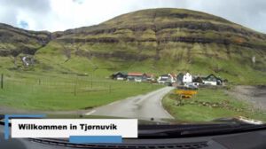 In Tjornuvik fährt ein Auto einen Hügel hinunter, im Hintergrund ein Berg.