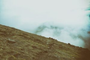 Eine Person geht mit Wolken im Hintergrund einen Hügel hinauf.