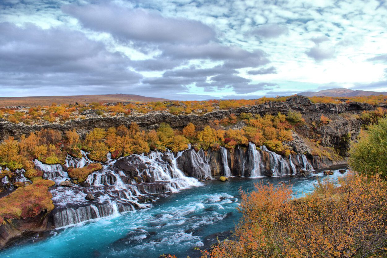 Ein Wasserfall in Island mit einem Regenbogen im Hintergrund.