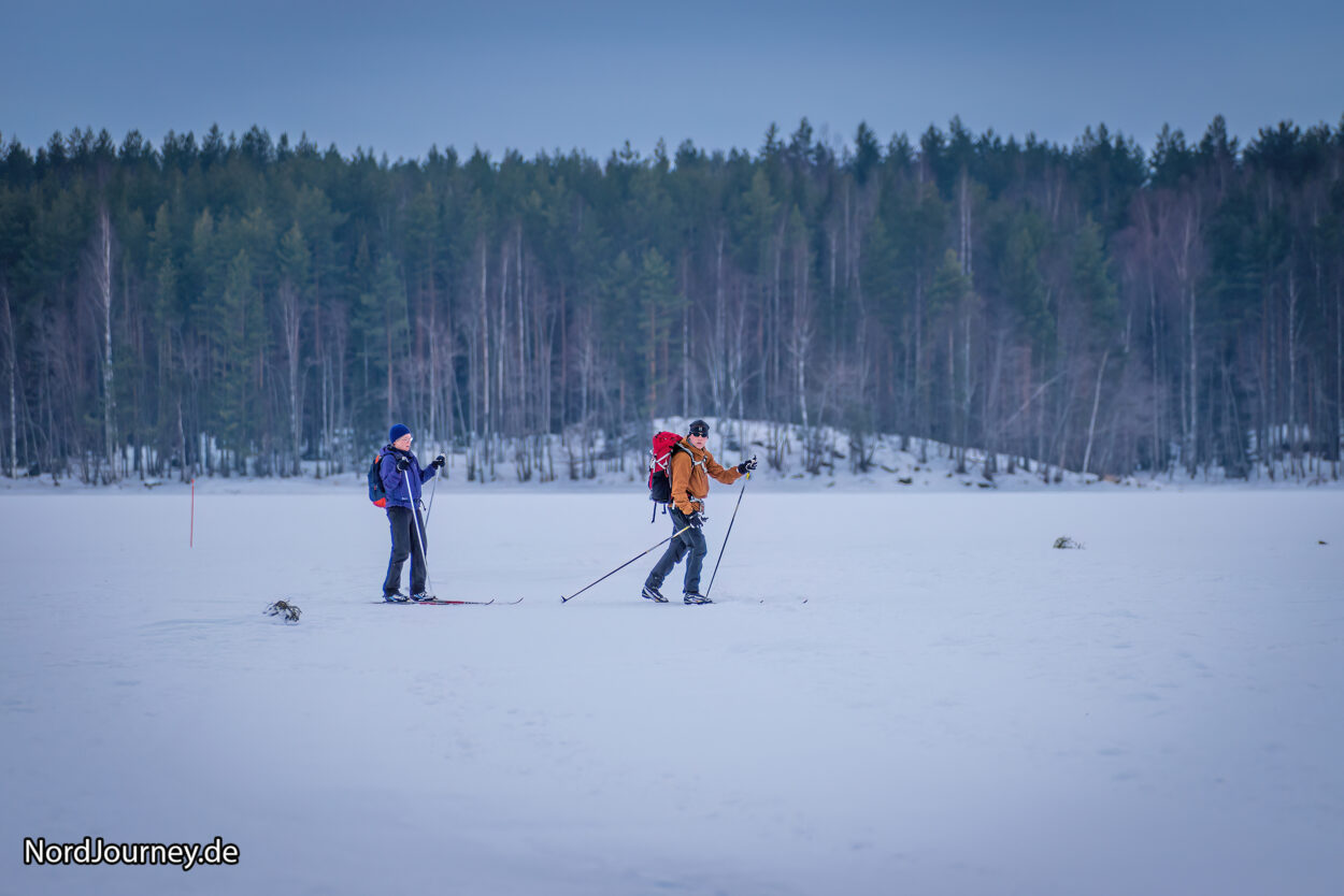 Zwei Personen laufen auf Skiern über ein verschneites Feld.