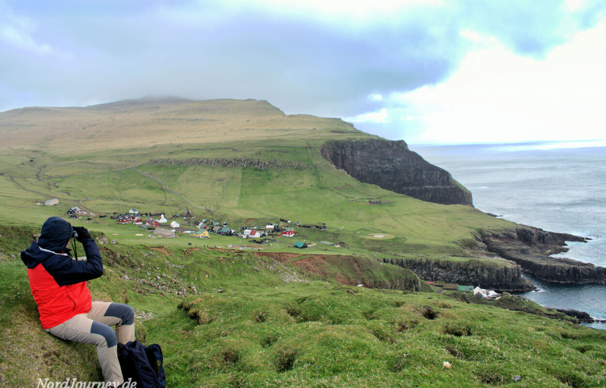 Eine Person sitzt auf einem Hügel und blickt auf das Meer.