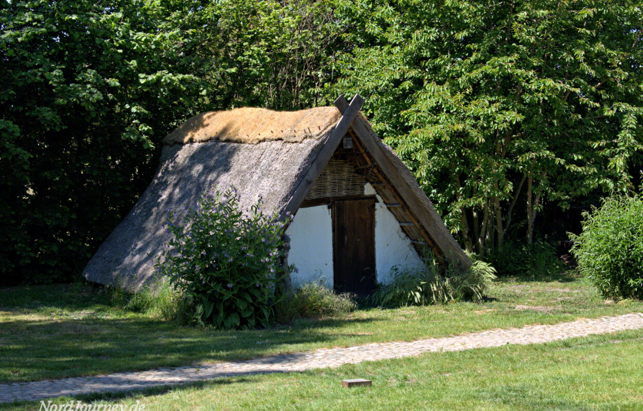 Ein Holzhaus mit Strohdach inmitten einer Wiese.