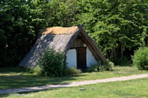 Ein Holzhaus mit Strohdach inmitten einer Wiese.