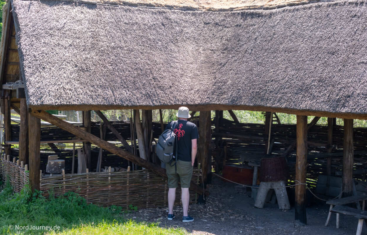 Ein Mann steht vor einer Hütte mit Strohdach.