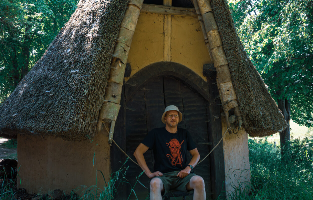 Ein Mann sitzt auf einem Stuhl vor einer strohgedeckten Hütte.