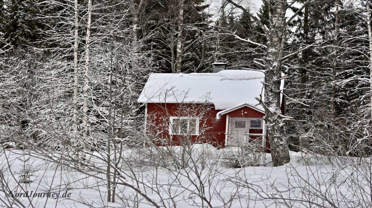 Ein kleines rotes Haus im Wald, bedeckt mit Schnee.