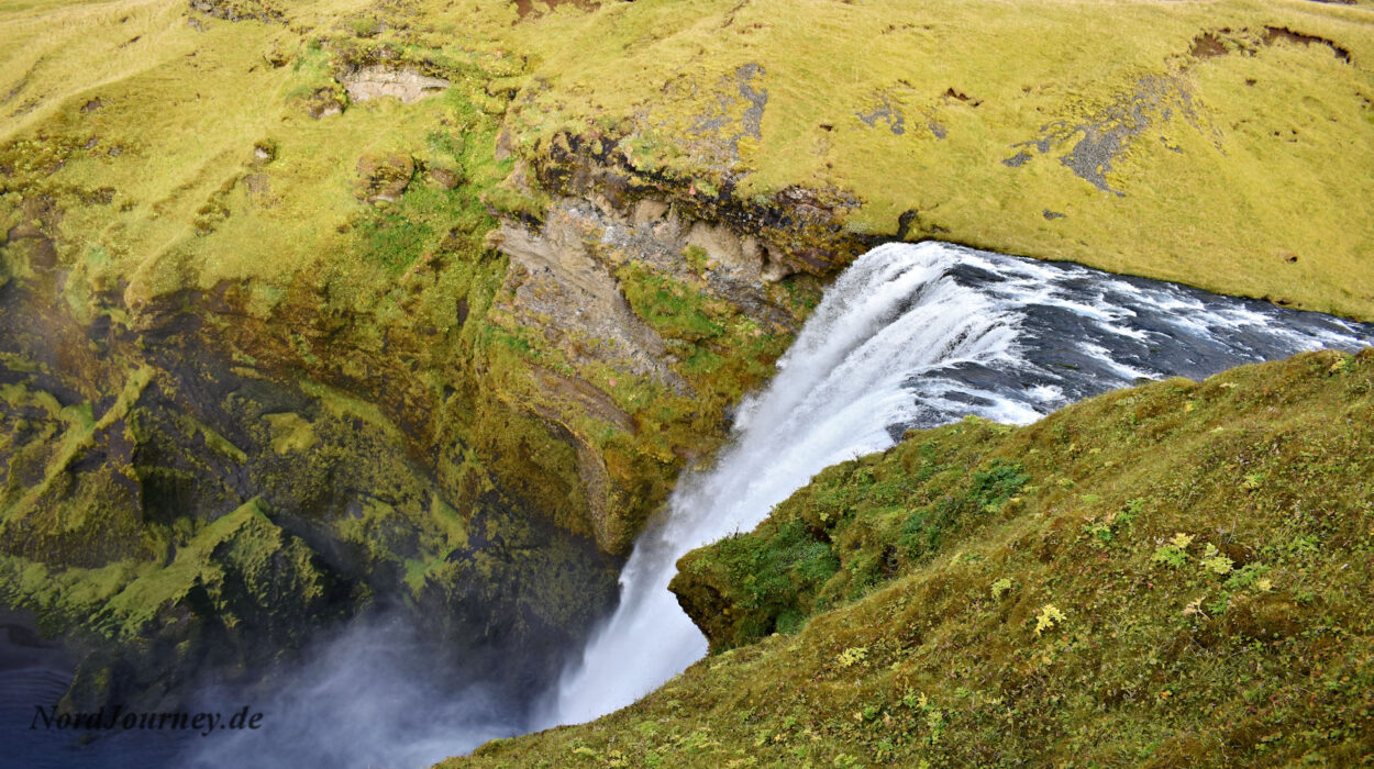 Ein Wasserfall inmitten einer grünen, grasbewachsenen Klippe.