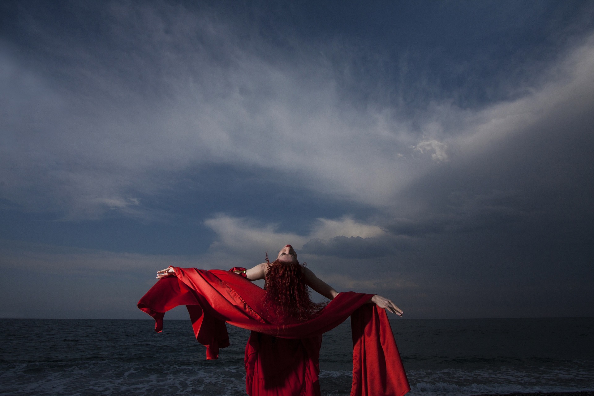 Eine Frau in einem roten Kleid, bewegt von der Faszination skandinavischer Musik, steht am Strand.