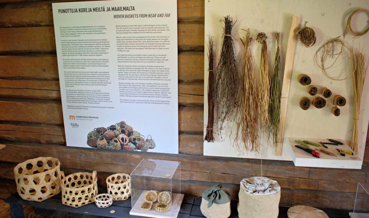 Ausstellung mit geflochtenen Körben mit beschreibenden Postern und Naturmaterialien auf einer Holzwand.