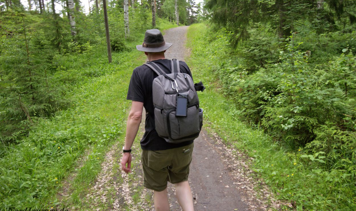 Person mit Hut, die mit einem Rucksack auf einem Waldweg wandert.