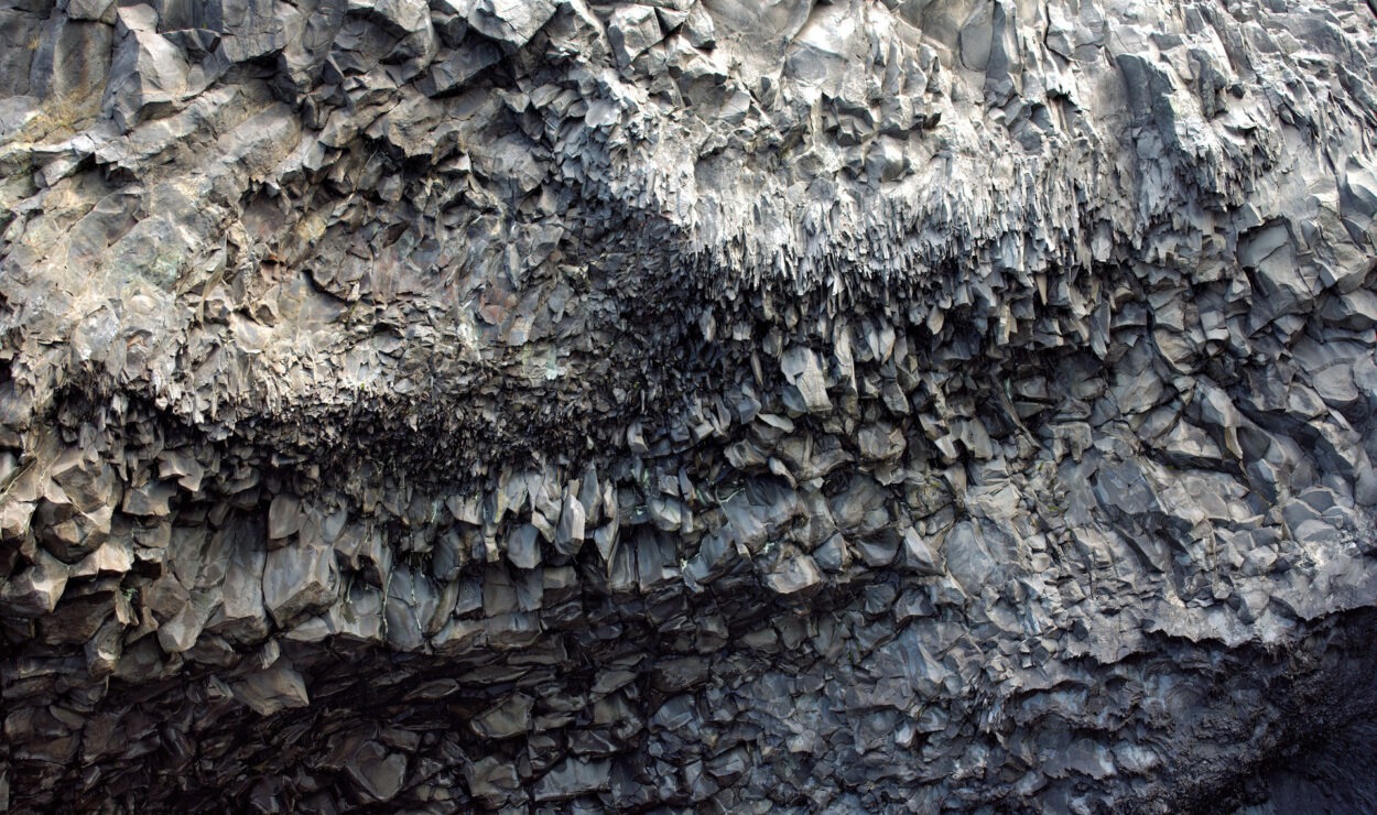 Nahaufnahme einer zerklüfteten, strukturierten Basaltfelsformation mit scharfen, eckigen Merkmalen, die an eine natürliche Höhlendecke erinnert.