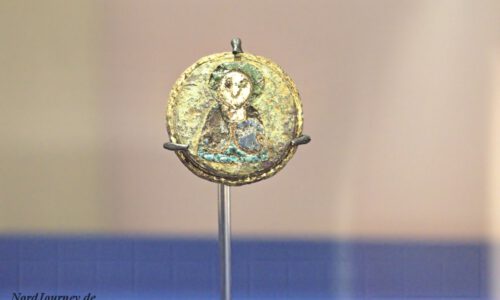 Ein rundes, gealtertes Medaillon mit dem verblassten Bild einer Figur in Robe, aufrecht auf einem Ständer vor einem schlichten Hintergrund ausgestellt.
