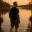 Ein Foto eines weißen Mannes mittleren Alters mit Rucksack, der im seichten Wasser eines Sees steht und den Sonnenuntergang betrachtet, im Hintergrund sind Bäume am Ufer zu sehen.