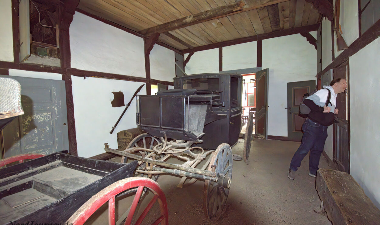 Ein Mann betrachtet eine Ausstellung in einem historischen Kutschenhaus mit zwei alten Holzkutschen darin.