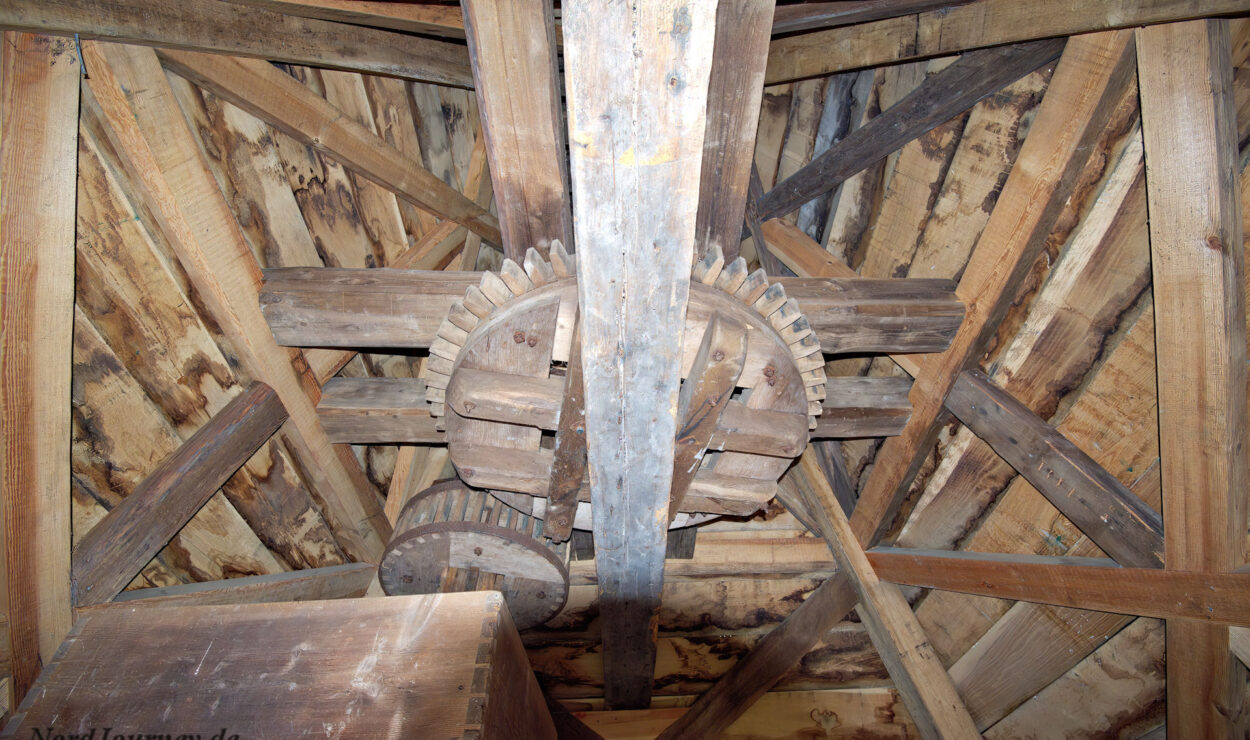 Holzzahnräder und -balken, die Teil des Dachmechanismus einer alten Mühle sind, von unten betrachtet, mit sichtbaren Holzstrukturen und -verbindungen.