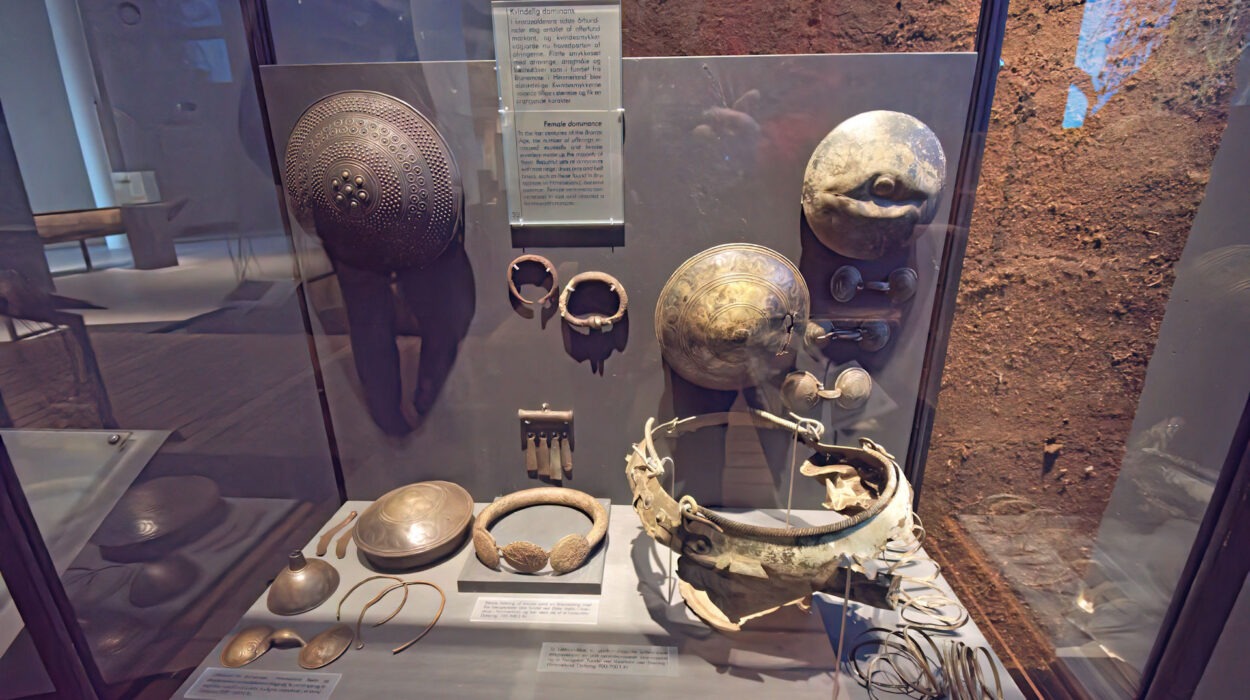 Eine Museumsvitrine mit antiken Metallartefakten, darunter verzierte Schilde, Armbänder, Schalen, eine Krone und verschiedene Schmuckstücke mit beschreibenden Etiketten.