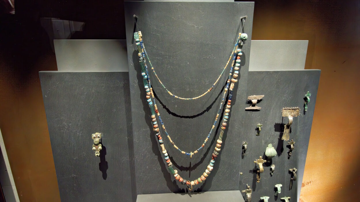 Ausstellung von antikem Schmuck, einschließlich Perlenketten und verschiedenen kleinen Anhängern und Artefakten, die auf einem gestuften schwarzen Ständer angeordnet sind.